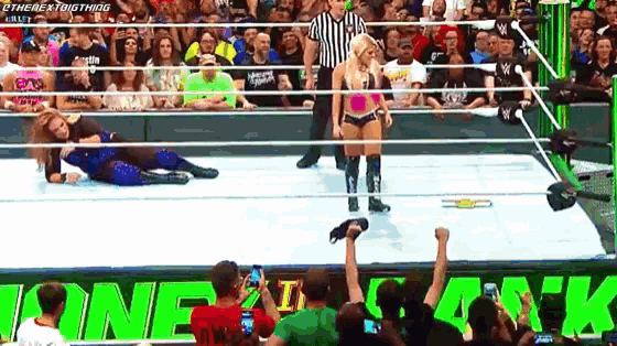 a woman is standing in a wrestling ring in front of a crowd that is watching a match between two women .