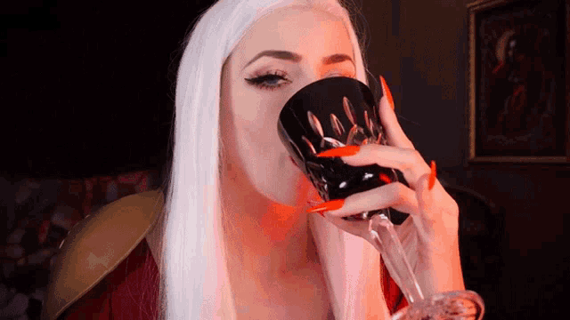 a woman with long red nails is drinking from a goblet