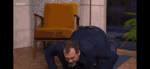 a man in a suit is doing push ups on a yoga mat in front of a chair with bbc written on it