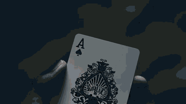 a person is holding an ace spades playing card in their hand