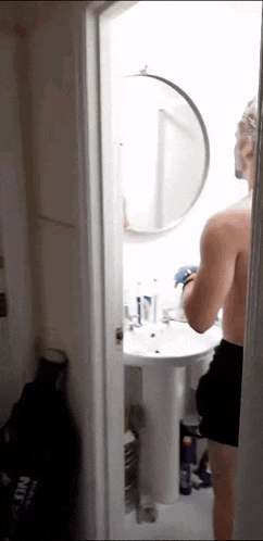 a man without a shirt is standing in a bathroom looking at himself in a mirror