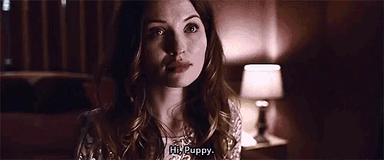 a woman is sitting in a dark room with a lamp and talking to a puppy .
