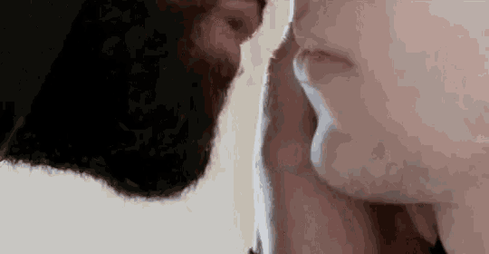 a man with a beard is touching another man 's face .