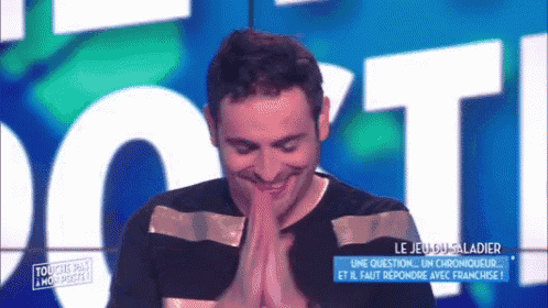 a man is smiling with his hands folded in front of a sign that says t