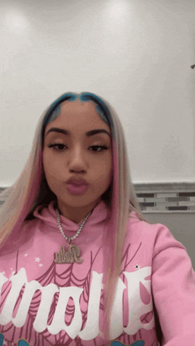 a girl wearing a pink hoodie and a necklace is taking a selfie .