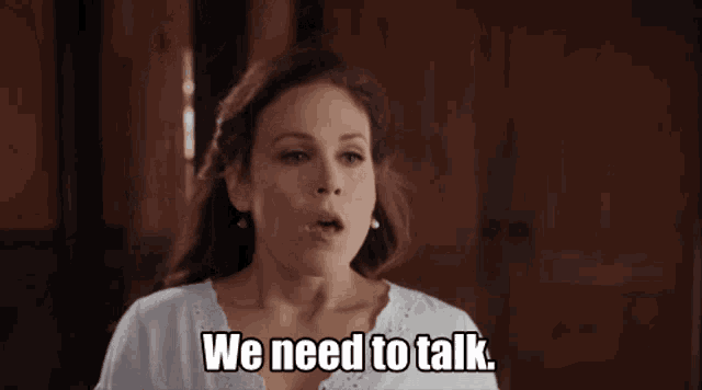 a woman says " we need to talk " in front of a wooden wall