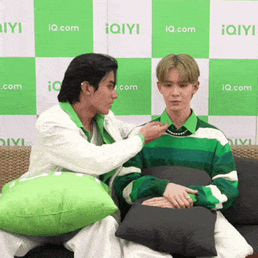 two men sitting on a couch in front of a wall with iq.com written on it