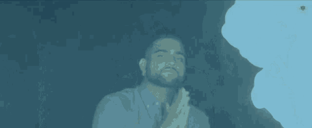 a man in a blue shirt with his hands folded in front of a fire