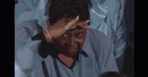 a man in a blue shirt is covering his face with his hand and looking at the camera .