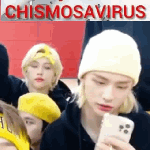 a man wearing a yellow hat is holding a cell phone in front of a group of people .