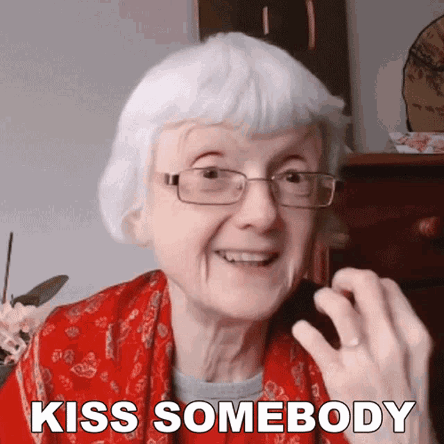 an elderly woman with glasses and a red scarf says kiss somebody
