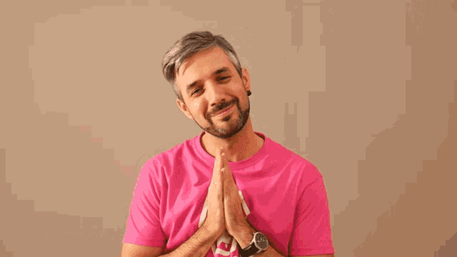 a man wearing a pink shirt and a watch holds his hands to his chest