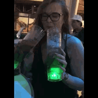 a woman is drinking from a green glass that says heineken