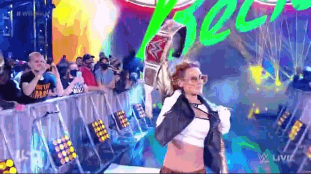 a woman is holding a championship belt while walking on a stage in front of a crowd .