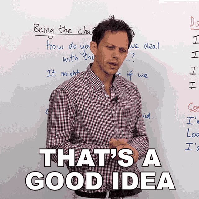 a man in a plaid shirt stands in front of a whiteboard that says being the chair