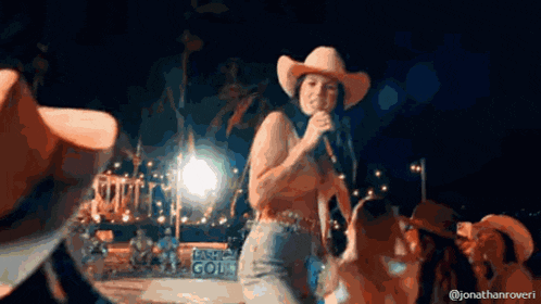 a woman wearing a cowboy hat is singing into a microphone .