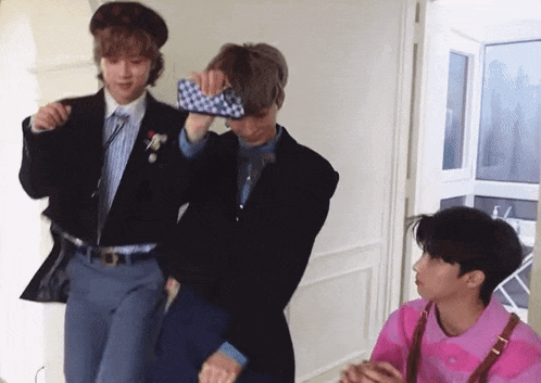 three young men are standing next to each other in a room and one of them is holding a cell phone .