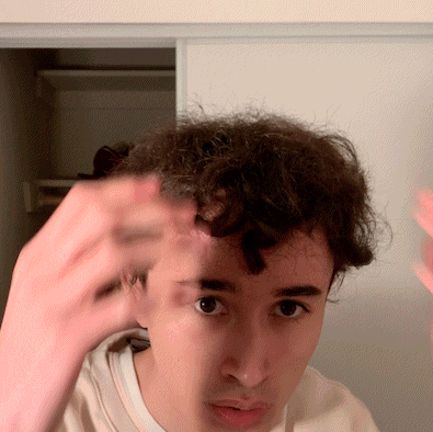 a man with curly hair looks at the camera with his hand on his forehead