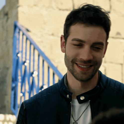 a man with a beard wearing a black leather jacket smiles
