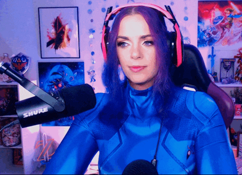 a woman wearing headphones and a blue suit stands in front of a shure microphone