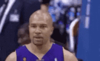 a bald basketball player wearing a purple jersey is standing in front of a blue wall .