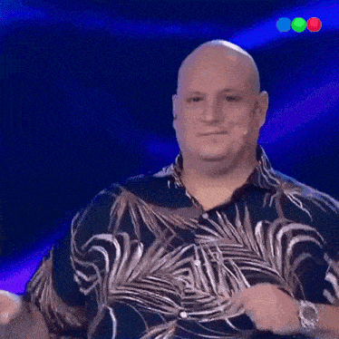 a bald man wearing a hawaiian shirt stands in front of a microphone