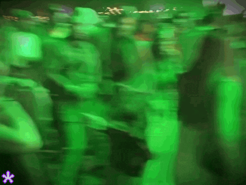 a blurry picture of people dancing in a green room with a purple flower in the corner