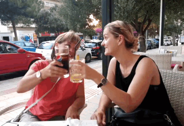 two women are sitting at a table toasting with beer glasses