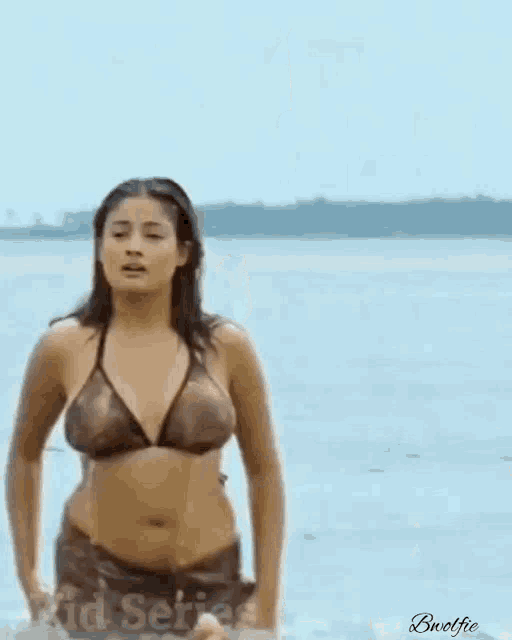 a woman in a bikini is walking on the beach in the rain .