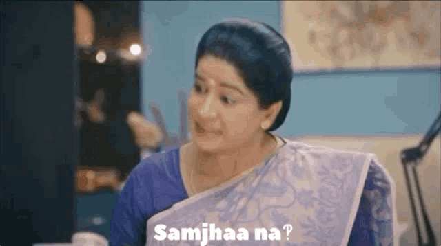 a woman in a blue saree is sitting at a table and smiling while talking to someone .