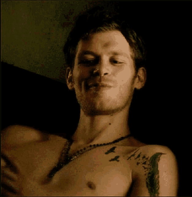 a shirtless man with a tattoo on his chest and a necklace is smiling .