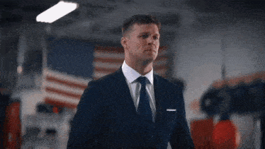 a man in a suit and tie is standing in front of an american flag in a gym .