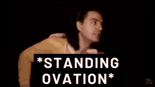 a man in a yellow jacket is standing in front of a sign that says standing ovation * .
