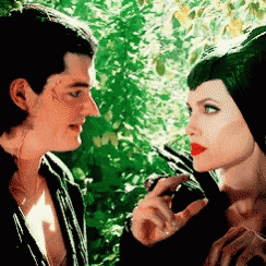 a man and a woman are looking at each other in front of trees .