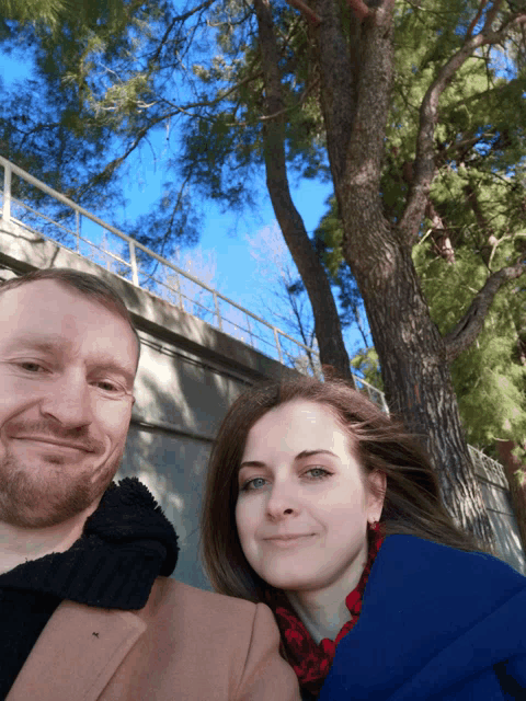 a man and a woman are posing for a picture in front of a tree