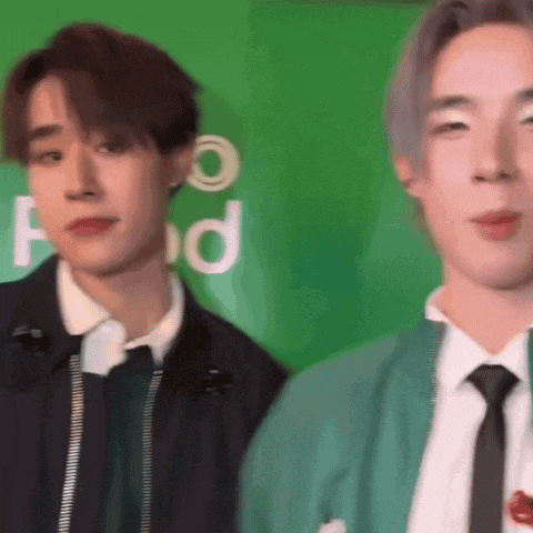 two men are standing next to each other in front of a green wall .