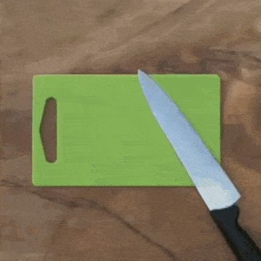 a person wearing a watch is cutting a green cutting board with a knife