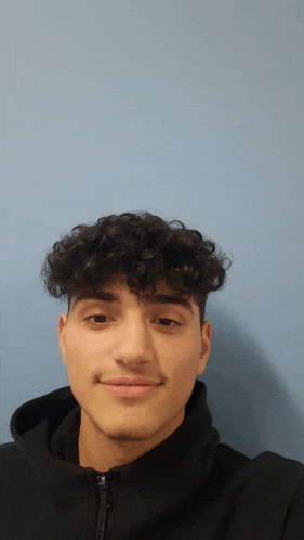 a young man with curly hair is wearing a black sweatshirt