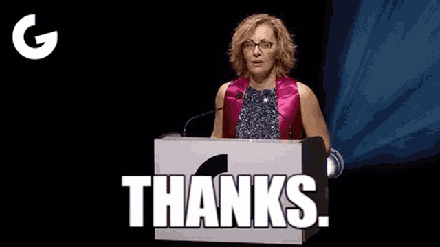 a woman is standing at a podium with a microphone and saying thanks .