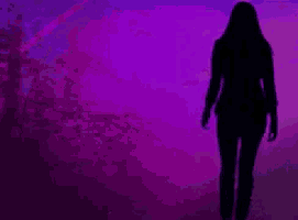 a silhouette of a woman walking in front of a purple sky .