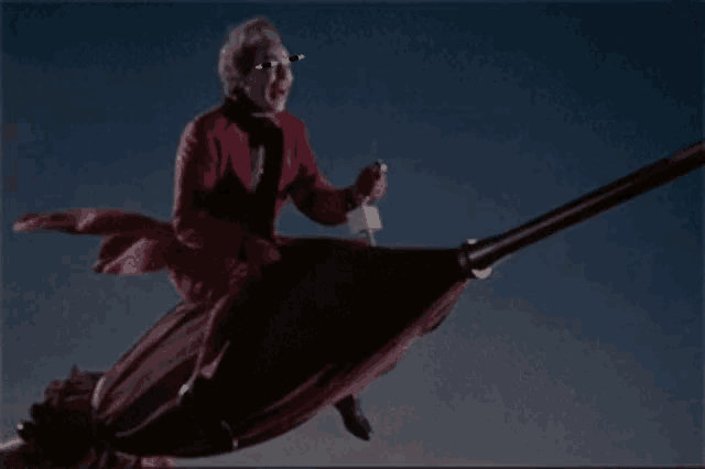 a man in a red suit is flying on a broom with sunglasses on
