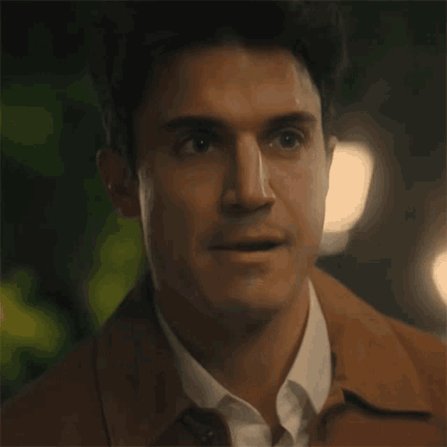 a close up of a man wearing a brown jacket and white shirt .