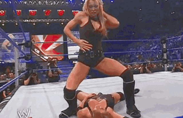 a woman is standing on top of a wrestler in a ring .