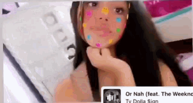 a girl with colorful stickers on her face is taking a selfie with a cell phone .