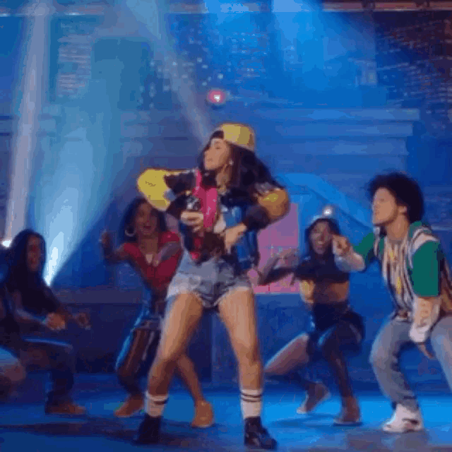 a group of people are dancing on a stage and one of them is holding a skateboard .