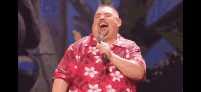 a man in a red shirt is singing into a microphone while laughing .