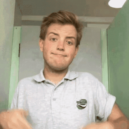 a young man in a grey polo shirt is making a funny face while standing in front of a green door .