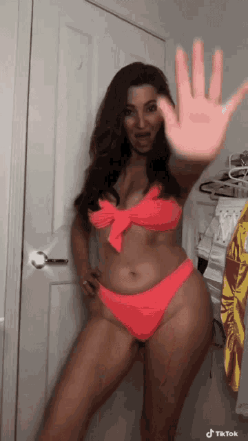 a woman in a pink bikini is standing in front of a door making a stop sign .