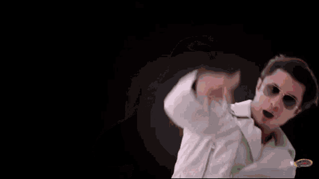 a man wearing glasses and a white shirt is standing in a dark room .
