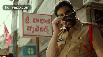 a man in a police uniform is wearing sunglasses in front of a sign that says ' shree balaji ' .